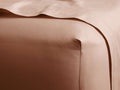 Smooth, clay-colored Italian Garment-Dyed Sateen Fitted Sheet pulled taut over a mattress corner, with a soft top sheet.