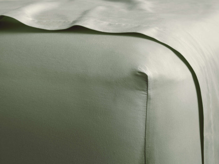 Close-up of a sage green Italian Garment-Dyed Sateen Fitted Sheet, smooth and subtly shimmering on a bed.