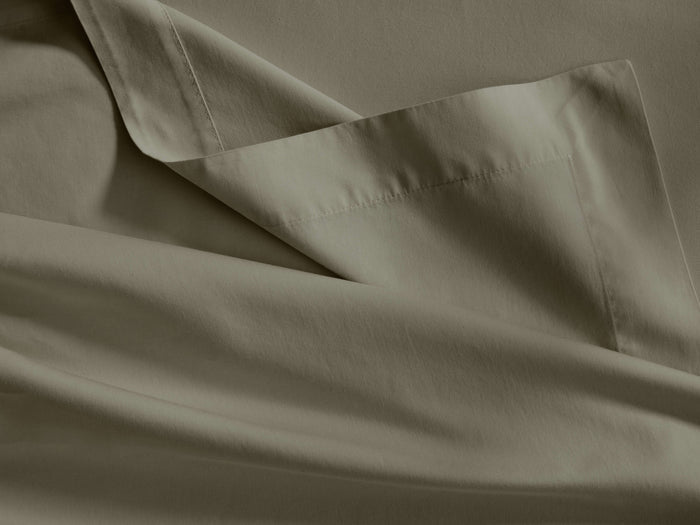 Close-up of an Italian Garment-Dyed Sateen Flat Sheet in muted sage green, showing its soft drapes, subtle sheen, and hem detail.