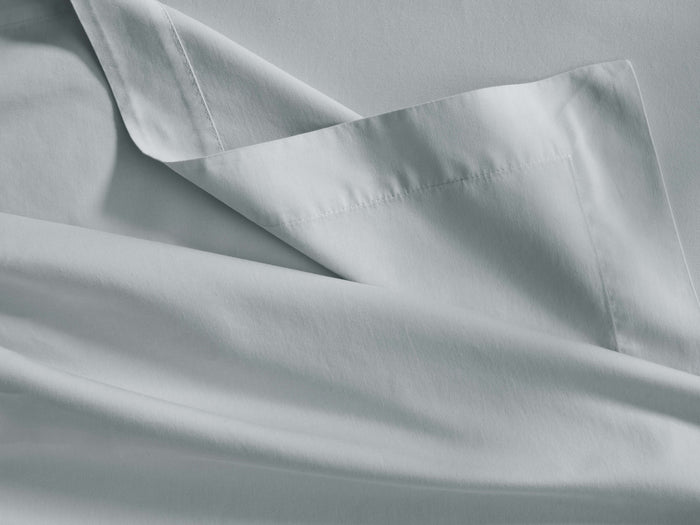 Close-up of a soft, sky-colored Italian Garment-Dyed Sateen Flat Sheet, gently folded, showing a stitched hem.