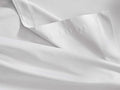 White Italian Garment-Dyed Sateen Flat Sheet, folded to reveal its smooth texture and a neat hemline stitching.