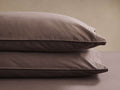 Two brown pillows stacked neatly on a brown surface, showcasing smooth fabric and fine stitching against a neutral background.
