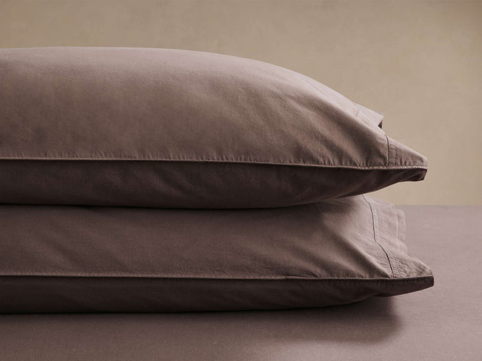 Two brown pillows stacked neatly on a brown surface, showcasing smooth fabric and fine stitching against a neutral background.