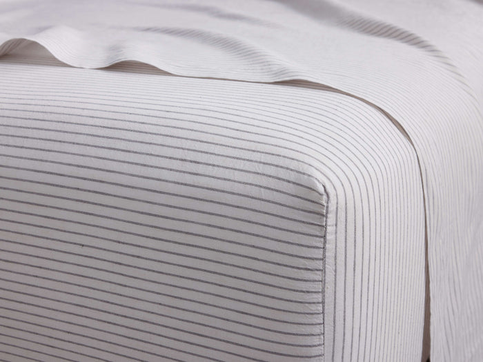 White Italian Yarn-Dyed Stripe Fitted Sheet on a bed. Thin gray stripes, horizontal on top, vertical on side.