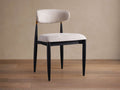 Jagger Dining Side Chair, angled, with black frame, light beige upholstered seat & curved back, gold accent, on wood floor.