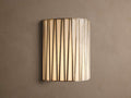 Jeunet Sconce, glowing, with vertical antiqued brass iron strips over translucent white glass, mounted on a neutral wall.