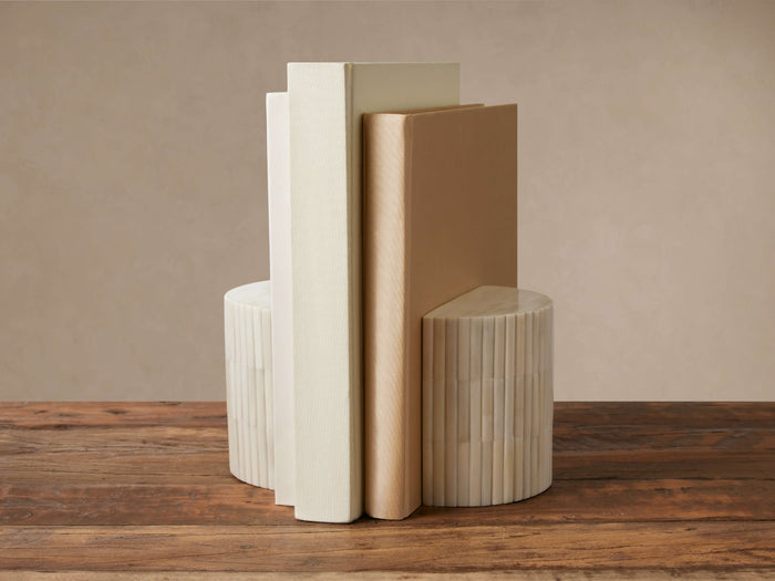 Jimena Bookends: Two ivory ribbed bone inlay bookends, semicircular, holding three light-colored books on a wooden table.
