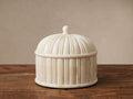 Jimena Lidded Jar: ivory bone inlay with a domed, ribbed lid and finial, on a rustic wooden table.