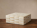 Jimena Striped Square Box: an ivory and beige striped bone inlay box, sitting on a rustic wooden table against a beige wall.