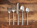 Kade Five Piece Place Setting: Polished stainless steel dinner fork, salad fork, knife, soup spoon, and teaspoon on rustic wood.