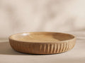Round Kanga Low Bowl, carved light mango wood with distinctive vertical ridges on exterior, smooth interior, on a light surface.