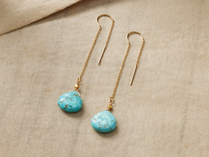 Two Kelby Drop Earrings: gold vermeil threader chains & teardrop turquoise stones with brown veining, on beige fabric.