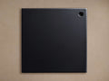Square black Kelly Finish Board with a subtle texture and a small circular hole in the upper right corner, against a tan background.