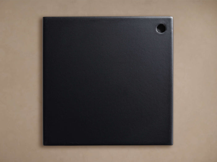 Square black Kelly Finish Board with a subtle texture and a small circular hole in the upper right corner, against a tan background.