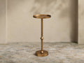 Kenneth Martini Table: Tall, hand-antiqued polished gold cast aluminum with round top, slender stem, and round base. On stone floor.