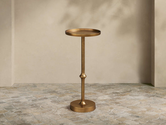 Kenneth Martini Table: Tall, hand-antiqued polished gold cast aluminum with round top, slender stem, and round base. On stone floor.