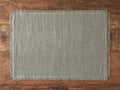 Khai Placemat shown on a wooden surface, featuring a woven texture in warm neutral tones with frayed edges for a rustic look.