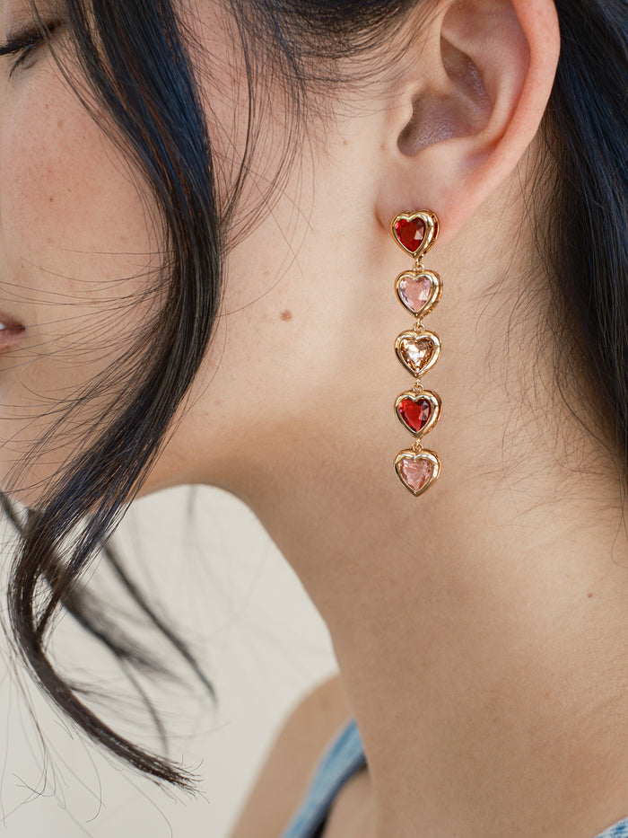 Close-up of a person wearing a set of pink heart-shaped earrings.