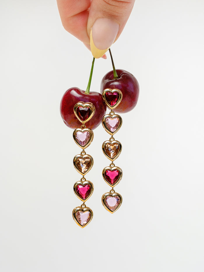 Heart-shaped earrings hanging from cherries against a white background
