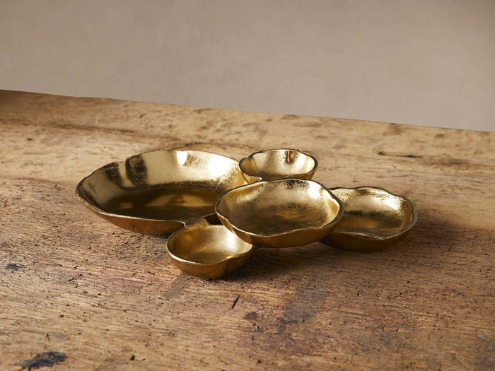 Five Klasa dark gold platters, varying organic shapes, clustered on a rustic wooden surface.