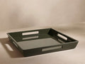 Square dark green tray with cut-out handles on each side, glossy finish, placed on a neutral surface, viewed from an angle.