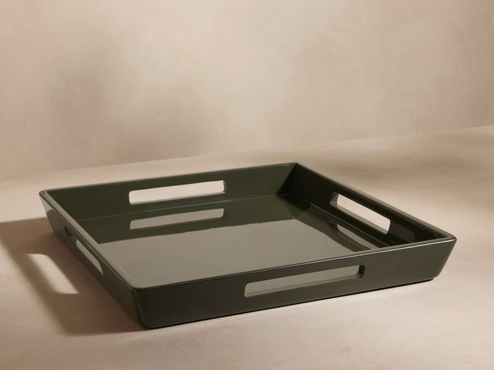 Square dark green tray with cut-out handles on each side, glossy finish, placed on a neutral surface, viewed from an angle.