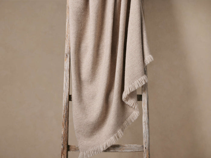 Landis Alpaca Throw, light beige with soft woven texture & fringe, draped over a rustic wooden ladder.