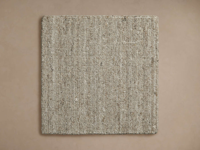 Lassen Rug Swatch: Light beige, square, handwoven natural fiber rug sample with visible texture, centered on a tan background.