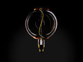 Clear glass globe bulb with amber tint and visible yellow filament inside. E26 base at bottom. Dark background highlighting bulb's design.