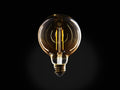 Amber glass LED G30 filament bulb with E26 base, glowing with warm light against a black background, highlighting its round shape and two-line filament.