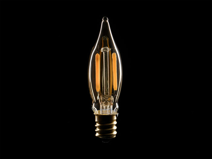 Front view of an LED Mini Filament E12 Bulb with amber glass, C18 shape, brass E12 base, and two vertical glowing orange filaments.