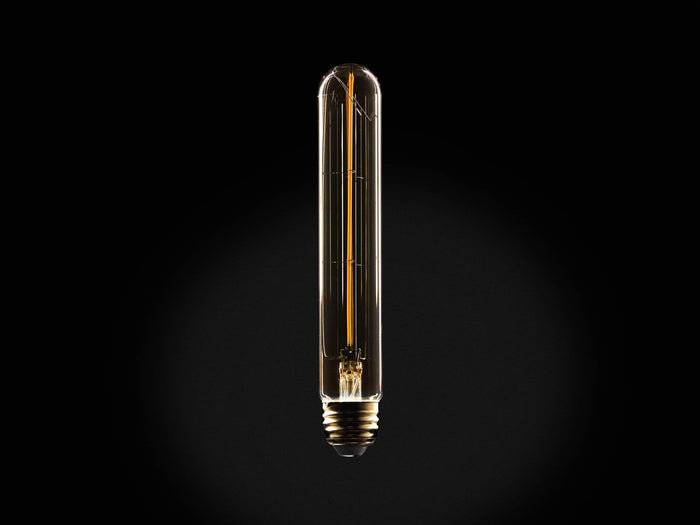 Front view of a vertical tubular Edison-style light bulb, clear glass, glowing amber filament, brass screw base.