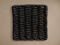 Black, rectangular Leon Outdoor Finish Board with a tightly woven texture, shown against a muted brown background.