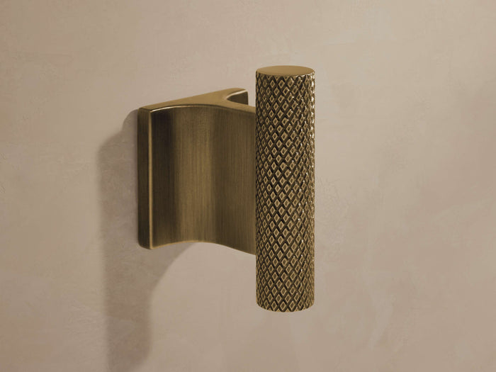 Liam Robe Hook in antique brass with knurled detailing on cylindrical hook, mounted on a flat rectangular base against a wall.
