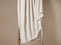 Light beige Lida Knit Throw with textured checkered pattern, draped over a rustic wooden ladder against a warm beige wall.