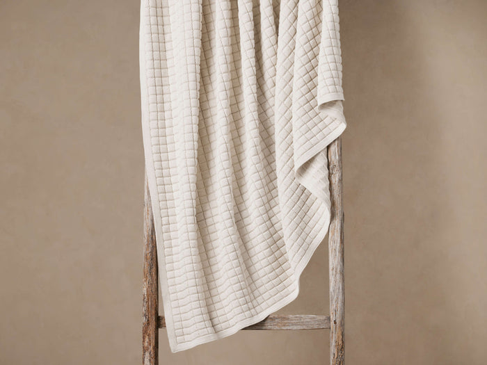 Light beige Lida Knit Throw with textured checkered pattern, draped over a rustic wooden ladder against a warm beige wall.
