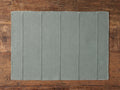 Linen Placemat in muted green with vertical stitched lines and frayed edges, laying flat on a wooden surface.