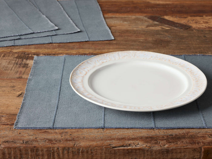 Linen Placemat on wooden table, pale blue with frayed edges, under a white plate. Three more placemats in the background.