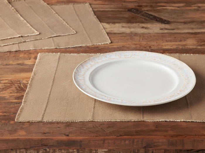 Overhead view of tan Linen Placemats (Set of 4) with frayed edges, subtle stripes, on a wooden table. One has a white plate.