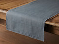 Linen Table Runner in a deep gray hue draped over a wooden table. Features a smooth texture and frayed edges along the sides.