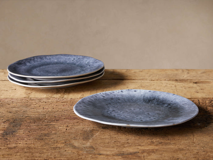 Set of 4 Luna Dinner Plates. Three stacked, deep blue reactive glazed plates with white undersides; one plate on rustic wood.