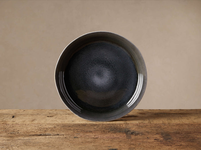Luna Round Platter, deep blue reactive glazed interior, soft white rim visible, standing on rustic wood against a tan wall.