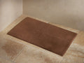 Luxe Turkish Bathmat in a rich brown color, placed on a tiled floor. The bathmat features a plush, soft texture and finished edge binding.