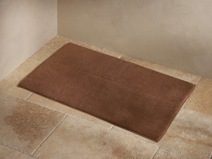 Luxe Turkish Bathmat in a rich brown color, placed on a tiled floor. The bathmat features a plush, soft texture and finished edge binding.
