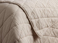 Close-up of a light beige Malea Cotton Quilt with a diamond quilted pattern, showing a folded edge and soft, crinkled texture.