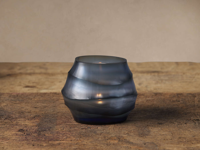 Deep blue Marella Tealight with wavy hand-cut texture, glowing candle inside, on a rustic wooden table.