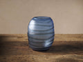 Deep blue Marella Vase, handcrafted glass with unique horizontal ripple textures, standing on a rustic wooden surface.