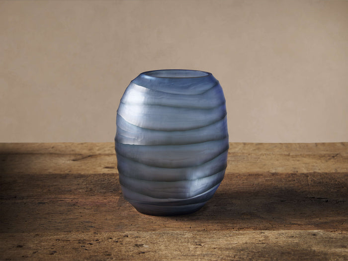 Deep blue Marella Vase, handcrafted glass with unique horizontal ripple textures, standing on a rustic wooden surface.