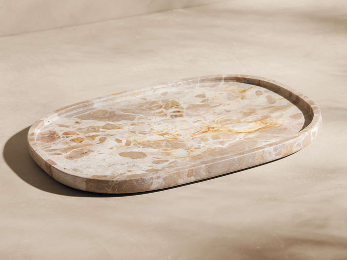 Mariyna Bath Tray: oval marble tray with natural beige, brown, and white veining, angled on a light background.