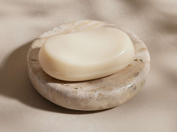 Mariyna Soap Dish: Round, beige marble with natural veining, holding an oval off-white soap bar, on a light neutral surface.
